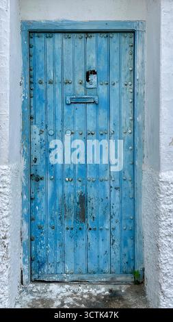Porte en bois bleu vieilli installée dans un mur en stuc blanc à Martil, Maroc. 15 octobre 2025. Banque D'Images