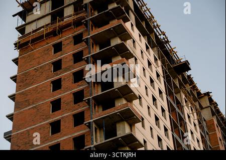 Un bâtiment résidentiel de plusieurs étages en construction en brique rouge et béton. Construction inachevée d'un immeuble de grande hauteur avec revêtement en briques Banque D'Images