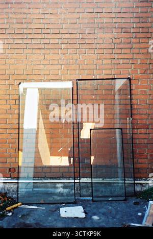 Verre d'une fenêtre enlevée appuyée contre un mur de briques rouges, reflétant le photographe. Film analogique. Banque D'Images