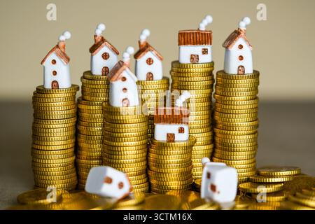 De minuscules modèles de maisons placés sur des piles de pièces d'or, symbolisant les prix de l'immobilier, les prêts hypothécaires, les tendances du marché du logement, l'épargne et l'investissement immobilier Banque D'Images