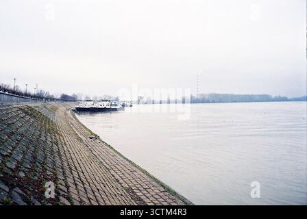 Rive du Danube en béton avec deux vieux bateaux amarrés à côté et une cheminée d'installation de chauffage lointaine, tourné sur un film couleur analogique nuageux. Banque D'Images