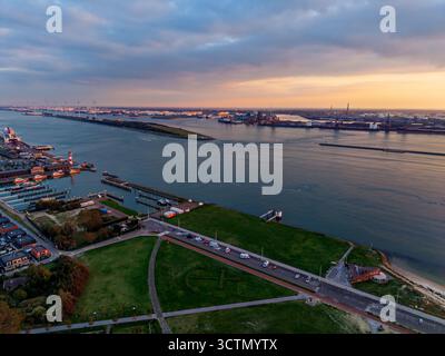 Vue aérienne du coucher du soleil sur les grues portuaires et les quais industriels bordent la rive éloignée, tandis que phare, bateaux, parc vert, et bâtiments de marina près de la rive Banque D'Images