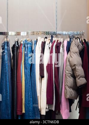 Gamme diversifiée d'articles de mode modernes d'automne et d'hiver sur un support de vente au détail. Présente les tendances actuelles en matière de vêtements décontractés, y compris le denim et les vêtements d'extérieur pour la saison. Photo verticale. Banque D'Images