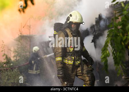 Un pompier professionnel en casque et combinaison de protection debout dans une fumée dense sur les lieux de l'incendie Banque D'Images