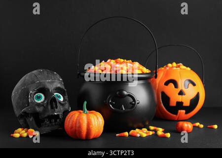 Chaudrons de savoureux cors de bonbons d'Halloween, crâne et citrouilles sur fond noir, gros plan Banque D'Images