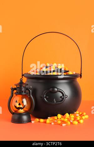 Chaudrons de savoureux cors de bonbons d'Halloween et lanterne sur fond orange Banque D'Images