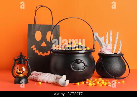 Chaudrons de cors de bonbons savoureux Halloween, os, sac en papier et lanterne sur fond orange Banque D'Images