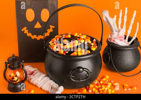Chaudrons de cors de bonbons savoureux Halloween, os, sac en papier et lanterne sur fond orange, gros plan Banque D'Images