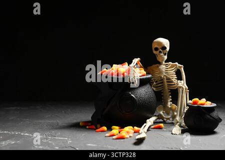 Chaudrons avec des cors de bonbons doux et squelette sur fond sombre. Célébration d'Halloween Banque D'Images