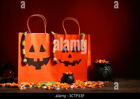 Chaudrons, sacs en papier et délicieux bonbons à la gelée d'Halloween sur la table en bois près du mur rouge Banque D'Images