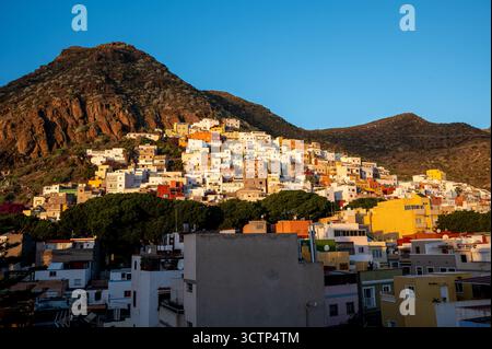 Vue aérienne de maisons aux couleurs vives descendant une pente montagneuse à San Andres, Tenerife. Baigné dans la lumière dorée du matin sous un ciel bleu Banque D'Images