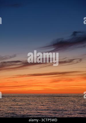 Vue imprenable sur l'océan au coucher du soleil. Avec des teintes orange et violettes vibrantes dans le ciel avec des ondes douces reflétant la lumière qui s'estompe. Création Banque D'Images