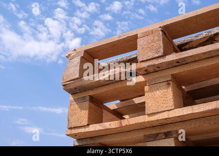 Vue rapprochée de plusieurs palettes en bois brut empilées à l'extérieur sous un ciel bleu vif avec des nuages dispersés. Mise en valeur du design industriel rustique et Banque D'Images