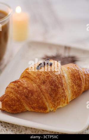 Délicieux croissant. Croissant fraîchement cuit sur une assiette à côté d'une tasse de café. Créer une scène de petit déjeuner chaleureuse et accueillante. Mise au point sélective. Banque D'Images