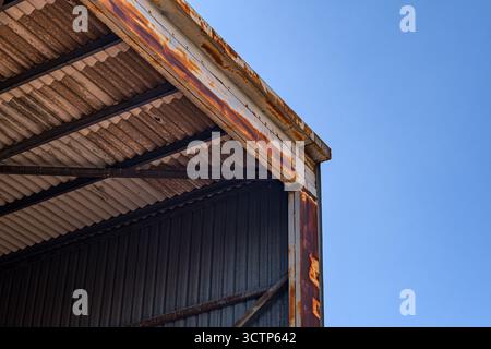 Toit d'entrepôt industriel rouillé contre le ciel dégagé. Vue détaillée d'une structure de toit d'entrepôt rouillée avec des panneaux métalliques ondulés. Capturer les personnes âgées Banque D'Images