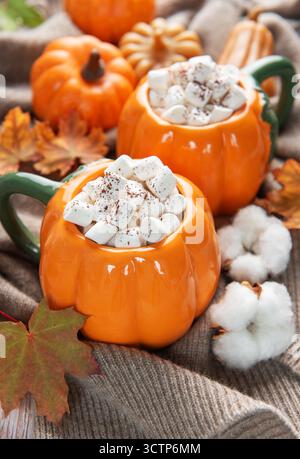 Deux mugs chauffants en forme de citrouille remplis de cacao et de guimauves sur un pull confortable avec un décor d'automne Banque D'Images