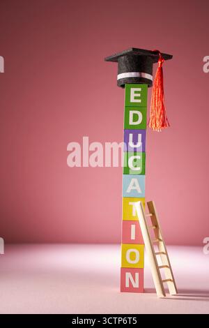 petit mortarboard sur le dessus des blocs de jouet colorés avec l'éducation de mot unique et l'échelle sur fond rose. Banque D'Images