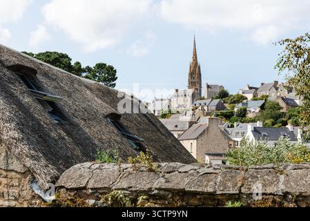 Un charmant cottage de chaume se trouve à côté d'un mur altéré, avec le village pittoresque de Pont-Croix, en Bretagne, et une grande flèche d'église dans l'arrière-pays Banque D'Images