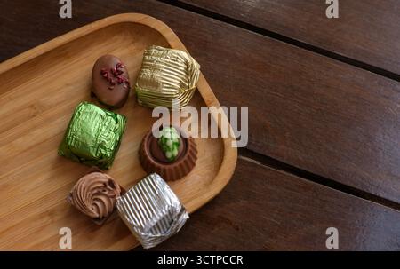 Chocolats assortis sur plateau en bois. Gros plan de chocolats assortis emballés et déballés placés soigneusement sur un plateau en bois de bambou au-dessus d'un t en bois rustique Banque D'Images