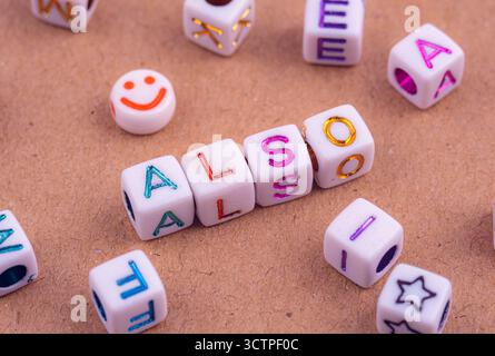 Perles alphabétiques colorées disposées pour épeler 'ALSO' sur une surface texturée. Les cubes sont entourés d'autres cubes de lettres dispersées et d'une perle de visage souriant. A Banque D'Images