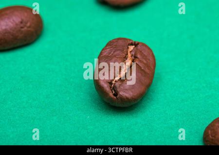 Plan macro d'un grain de café torréfié sur fond vert. La texture détaillée et la fissure soulignent la fraîcheur et l'arôme. Symbolisant la caféine. Banque D'Images