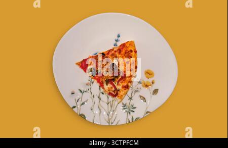Une seule tranche appétissante de pizza avec une présentation unique. Généreusement garni de pepperoni, d'olives et de poivrons, il repose sur une assiette blanche décorative Banque D'Images