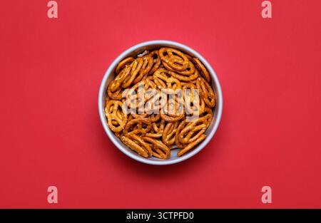 Vue de dessus d'un bol rempli de bretzels salés croustillants placés sur un fond rouge vif. Le snack doré cuit au four contraste. Banque D'Images