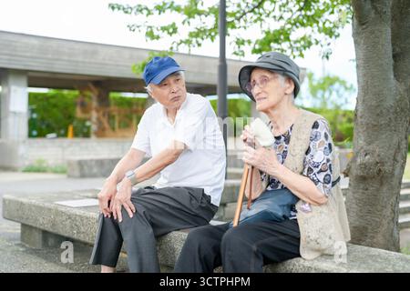 Deux personnes âgées sont assises sur un banc, l'une d'elles tenant une canne. Ils semblent profiter de la compagnie de l'autre et prendre une pause de leur quotidien Banque D'Images
