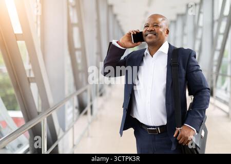 Homme d'affaires afro-américain confiant parlant au téléphone, transportant une mallette à l'aéroport Banque D'Images