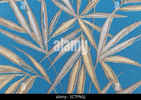 Feuilles de palmier tropical sur textile bleu - élégant fond de motif de feuillage doré Banque D'Images