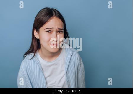 Jeune femme avec une expression confuse sur un fond bleu. Banque D'Images