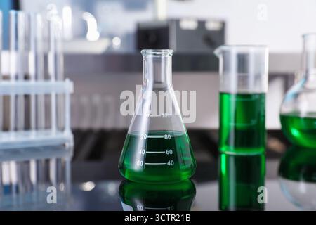 Flacon en verre et autre verrerie avec liquide vert sur table en laboratoire, gros plan Banque D'Images