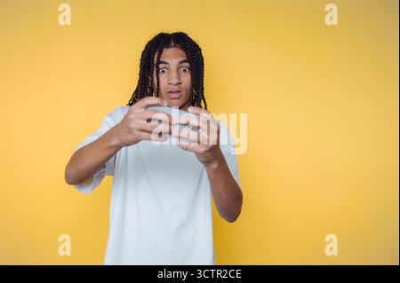 Jeune homme avec des dreadlocks jouant à des jeux vidéo, fond jaune. Banque D'Images