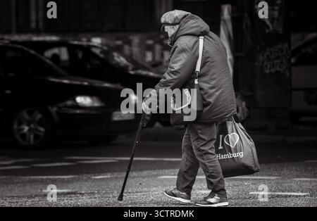 Homme âgé marchant avec la canne dans la scène de rue urbaine – photographie éditoriale en noir et blanc de Hambourg Allemagne Banque D'Images