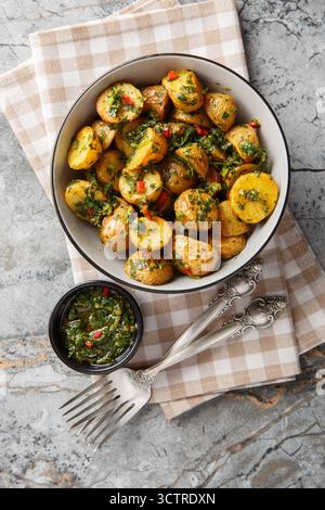 Pommes de terre nouvelles cuites au four servies avec une sauce chimichurri fraîchement préparée en gros plan dans un bol sur la table. Vue de dessus verticale Banque D'Images