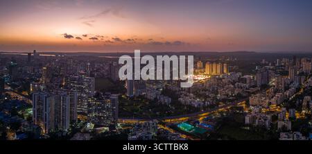 Vue aérienne du paysage urbain avec des bâtiments illuminés projetant une lueur chaude sur le ciel crépusculaire, mettant en valeur l'étalement urbain, Mumbai, Maharashtra, Inde. Banque D'Images