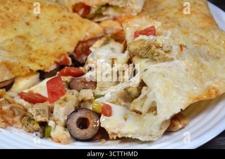 Une assiette de sandwich Pizza rempli de poulet avec des morceaux de tomate, poivre, olive, fromage mozzarella, sauce tomate dans un sandwich Banque D'Images