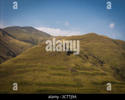 Vue aérienne d'anciennes structures en pierre nichées dans les collines vertes et brunes ondulantes sous un ciel bleu vif, Dartlo, Kakheti, Géorgie. Banque D'Images