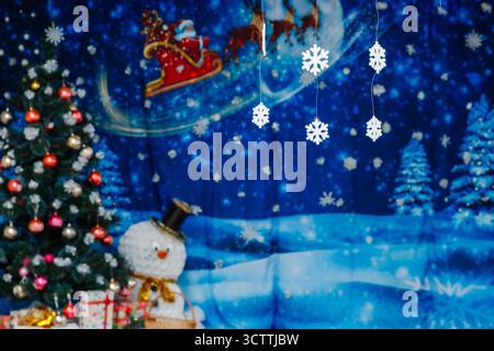 Composition de Noël avec un sapin de Noël décoré, un bonhomme de neige et des flocons de neige suspendus sur un fond bleu festif et une image du vol du Père Noël Banque D'Images