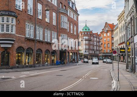 Une scène de rue animée avec des bâtiments danois classiques en briques rouges avec des toits à pignons et des fenêtres cintrées. Les piétons et les voitures passent Banque D'Images