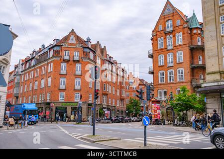 Une scène de rue animée avec des bâtiments danois classiques en briques rouges avec des toits à pignons et des fenêtres cintrées. Piétons, cyclistes et voitures qui passent Banque D'Images