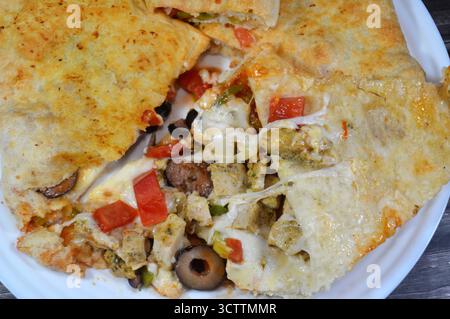 Une assiette de sandwich Pizza rempli de poulet avec des morceaux de tomate, poivre, olive, fromage mozzarella, sauce tomate dans un sandwich Banque D'Images