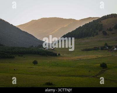 Vue aérienne du soleil projetant une lueur dorée sur les collines verdoyantes et les bâtiments dispersés d'Omalo, Kakheti, Géorgie. Banque D'Images