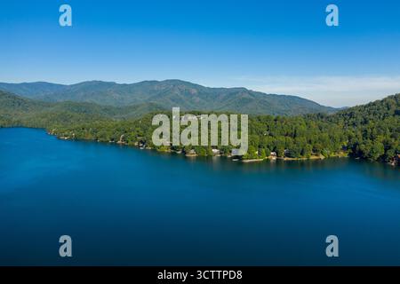 Vue aérienne des eaux sereines du lac rencontrant la forêt verdoyante le long du rivage, créant un contraste vibrant sous le ciel bleu clair, Lake Toxaway, Caroline du Nord, États-Unis. Banque D'Images