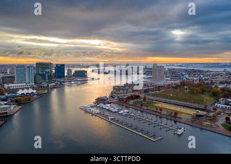 Vue aérienne du port intérieur reflétant la lumière de l'heure d'or, avec l'Aquarium national et la ligne d'horizon de la ville debout contre le ciel nuageux, Baltimore, Maryland, États-Unis. Banque D'Images