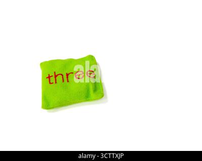 Sac de haricots vert vif avec le mot « Three » cousu en lettres rouges sur fond blanc. Ce jouet en tissu doux est couramment utilisé dans earl Banque D'Images