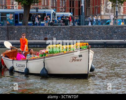 Amsterdam, pays-Bas - 5 août 2025 : deux femmes se détendent dans un bateau rempli de tulipes colorées tout en naviguant à travers Amsterdam. Banque D'Images