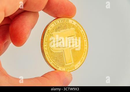 Image en gros plan d'une pièce de monnaie Tether tenue par une main, présentant le symbole B et un dessin en relief peut être utilisé dans des documents de marketing pour la crypto-monnaie, Banque D'Images