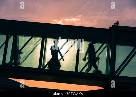 Groupe de passagers avec des bagages marchant à travers la passerelle d'embarquement à l'avion à l'aéroport. Silhouettes de personnes méconnaissables au coucher du soleil. Banque D'Images