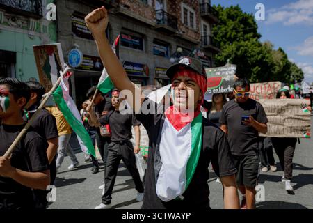 Un jeune militant marche dans une manifestation, portant un bandana aux couleurs palestiniennes et des lunettes de soleil, montrant son soutien à la cause. Banque D'Images